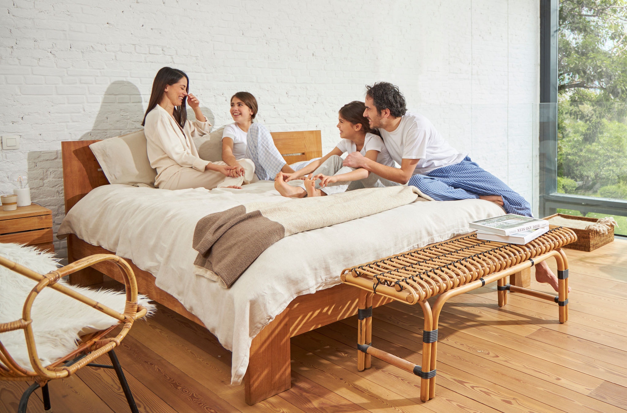 Жена и маж седат на кревет со две млади девојки, релаксирани и се смеат и уживаат во здрав воздух.