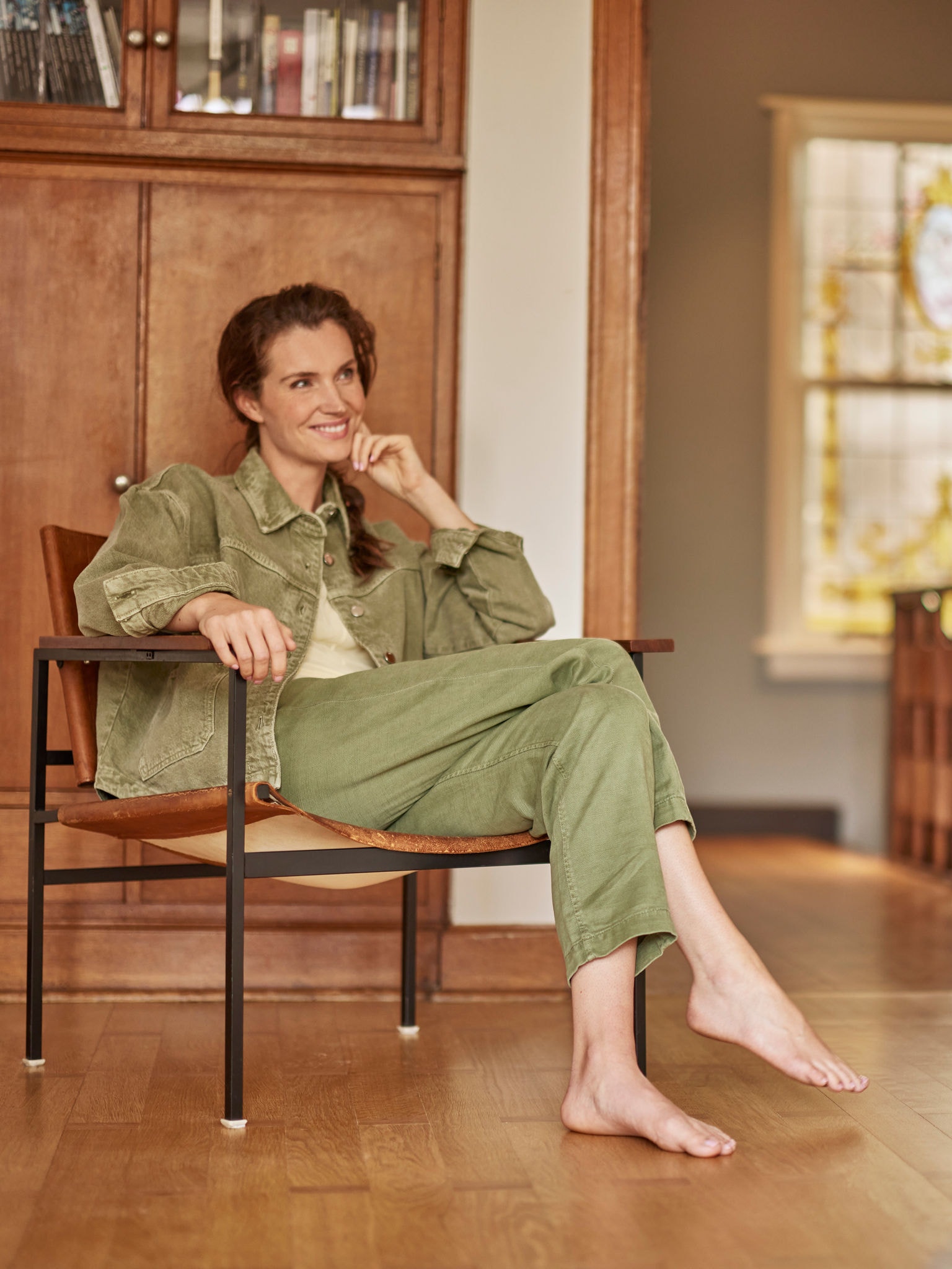 Жена седи во својата фотелја, боса, насмеана и гледа пред себе