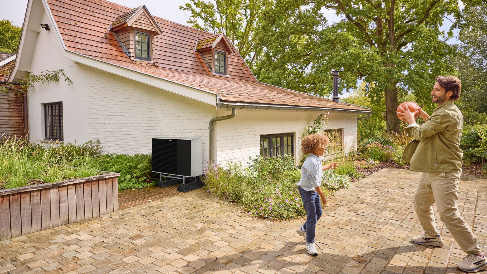 Татко и дете си играат со топка во дворот, со топлинска пумпа инсталирана во близина