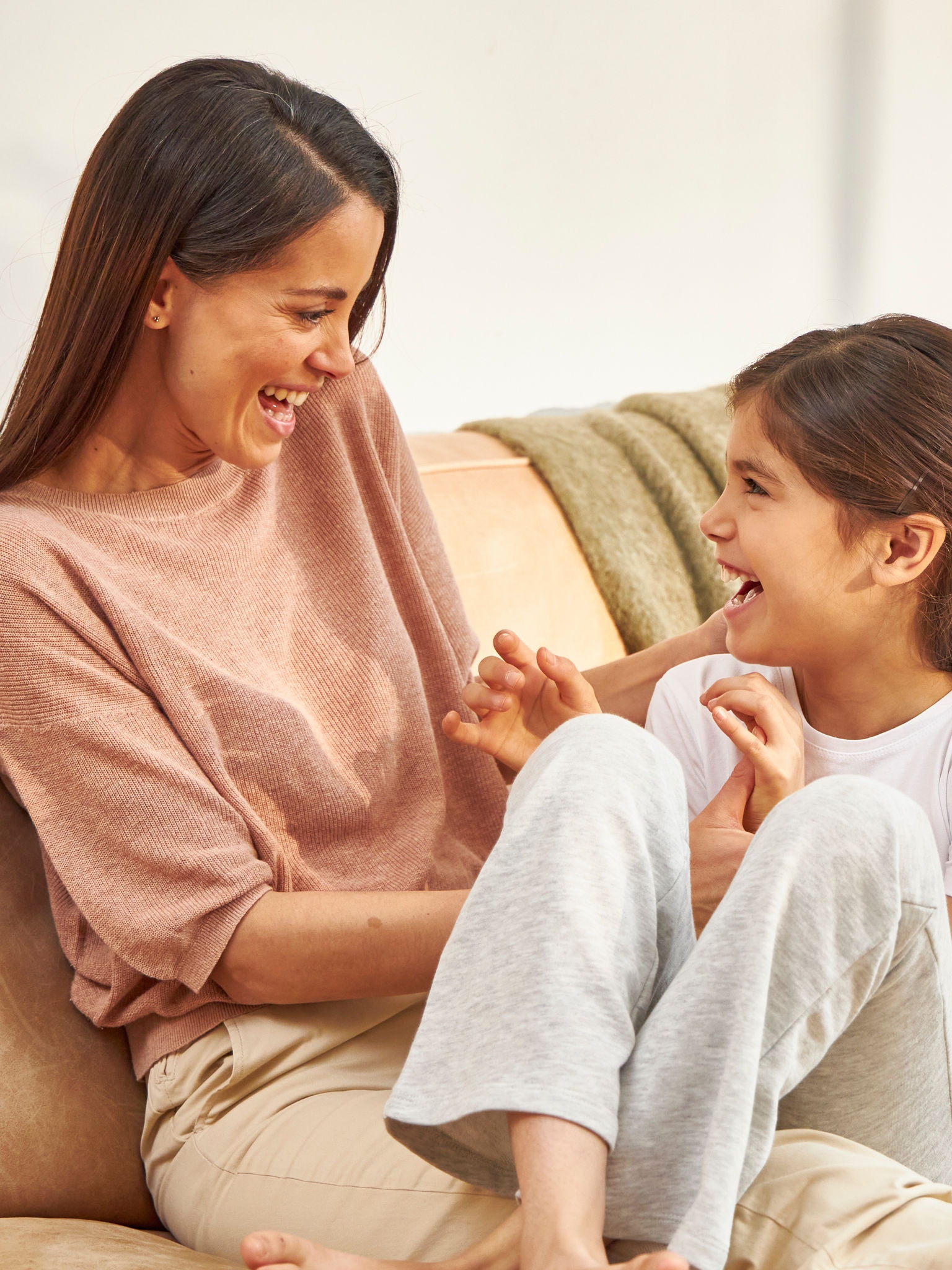 Возрасна жена седи меѓу две девојки на софа што се смеат и уживаат во здрав воздух.