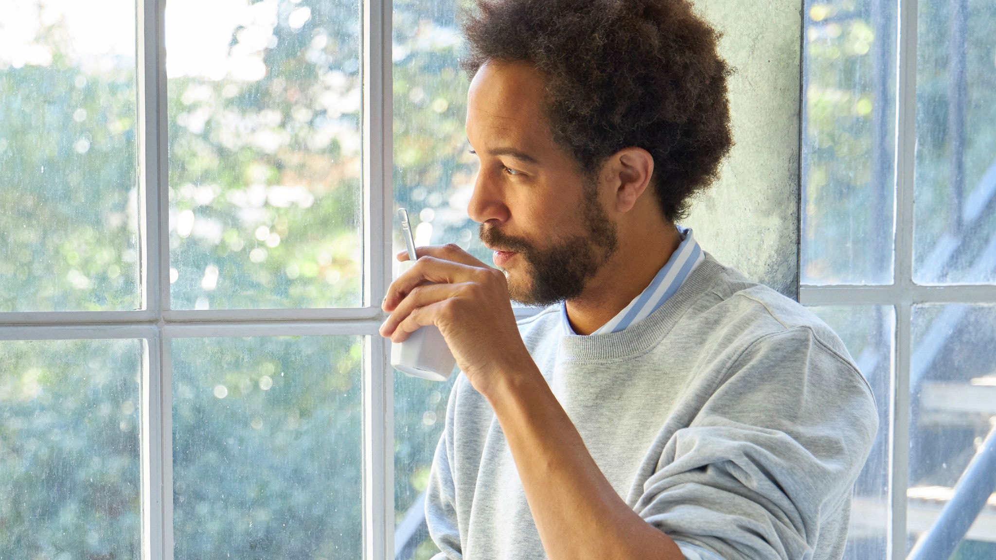 Човек пие од чаша до голем прозорец на сончево време
