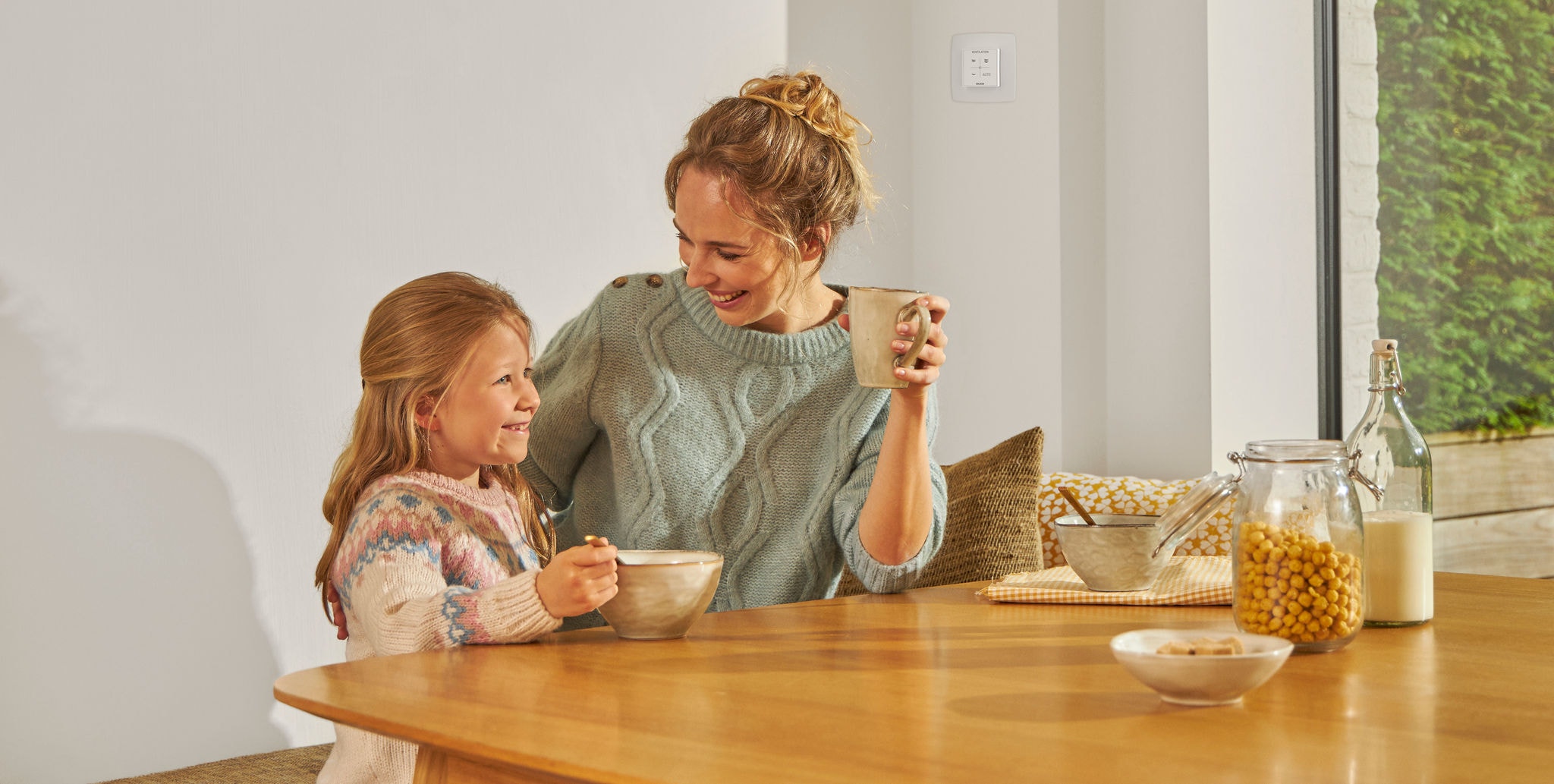 Млада девојка јаде од сад на масата до жена со шолја во раката, двете се смеат среќни и релаксирани и уживаат во здрав воздух.