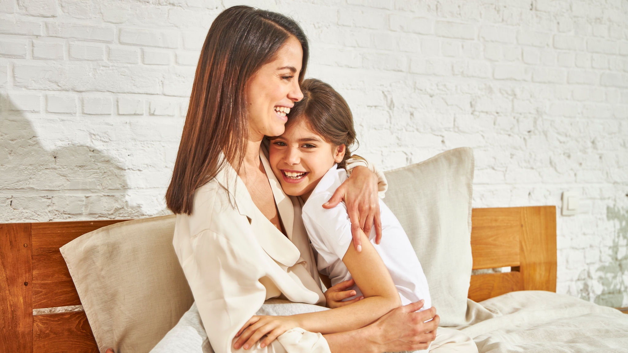 Мајка и ќеркичка се смеат и гушкаат додека седат на кревет