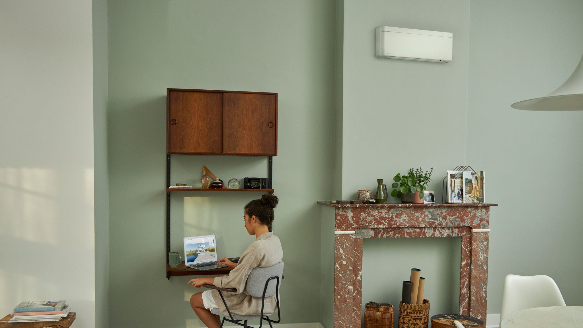 Жена го посетува центарот за виртуелно искуство на Daikin преку својот преносен компјутер на нејзиното мало биро, во прекрасно декорирана дневна соба